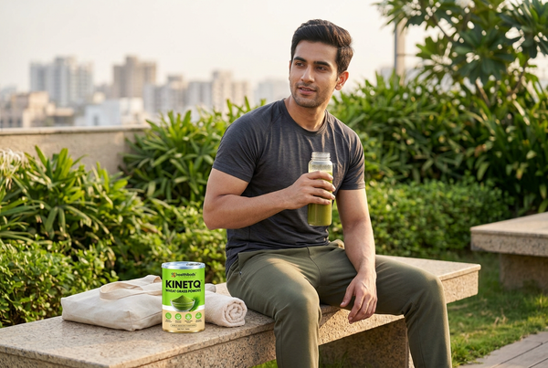 Man holding a green drink on a rooftop terrace beside a Healthibuds Wheatgrass Powder tin and canvas tote.